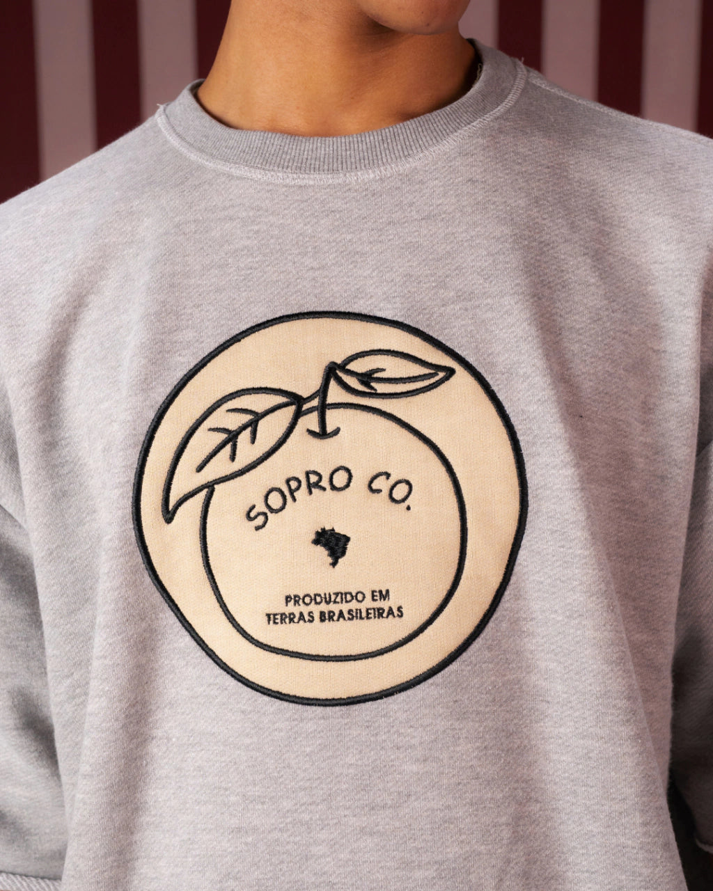 Moletom cinza com estampa redonda de laranja e texto "Sopro Co. Produzido em terras brasileiras"