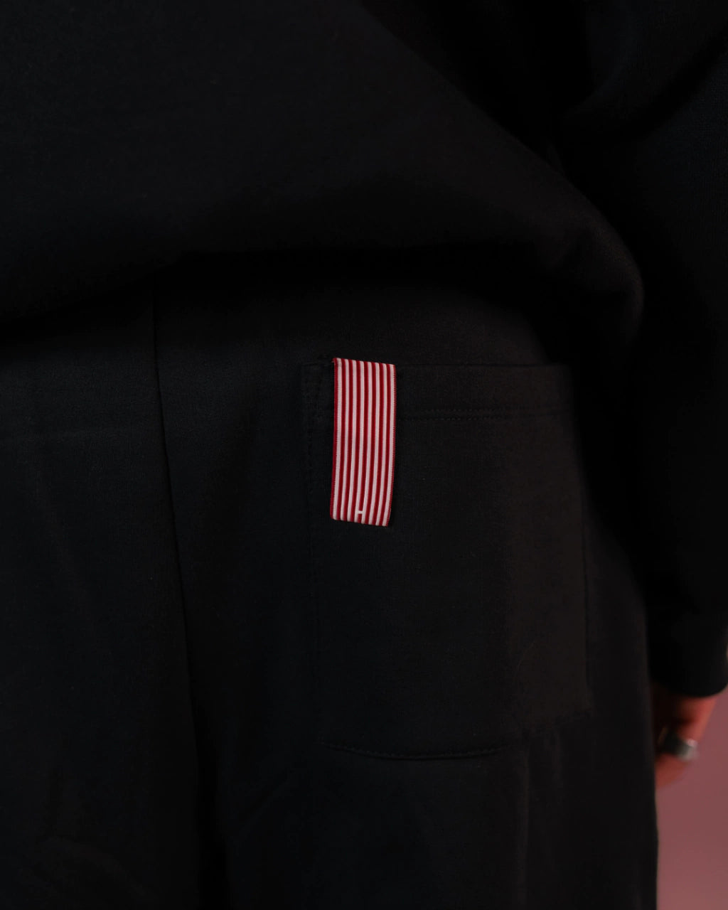 Detalhe da calça preta Precio com bolso traseiro e etiqueta listrada vermelha e branca