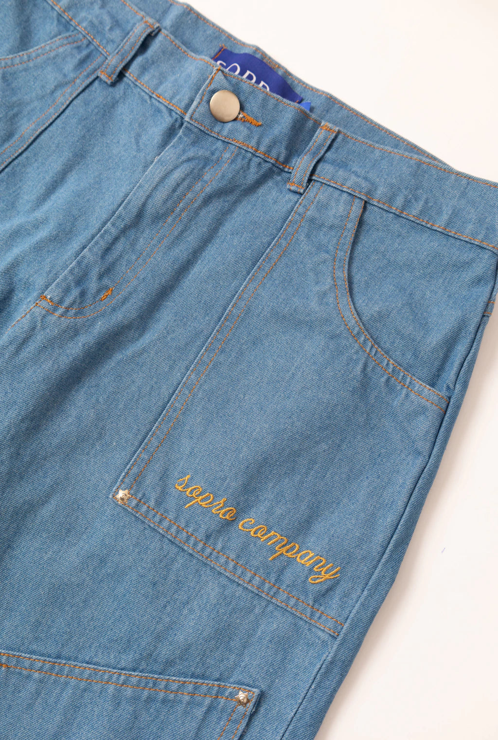 Detalhe da Calça Aporo Sulco em tecido jeans azul claro com costura laranja e bordado "aporo company" no bolso lateral